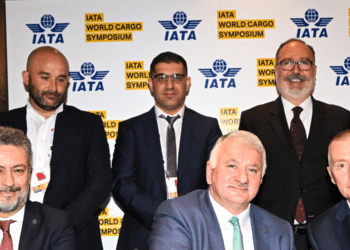 Eight men stand and sit in front of an IATA World Cargo Symposium backdrop.