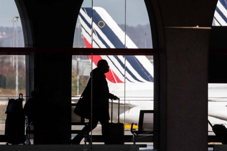 A passenger walks in a terminal in front of an Air France-KLM airplane.