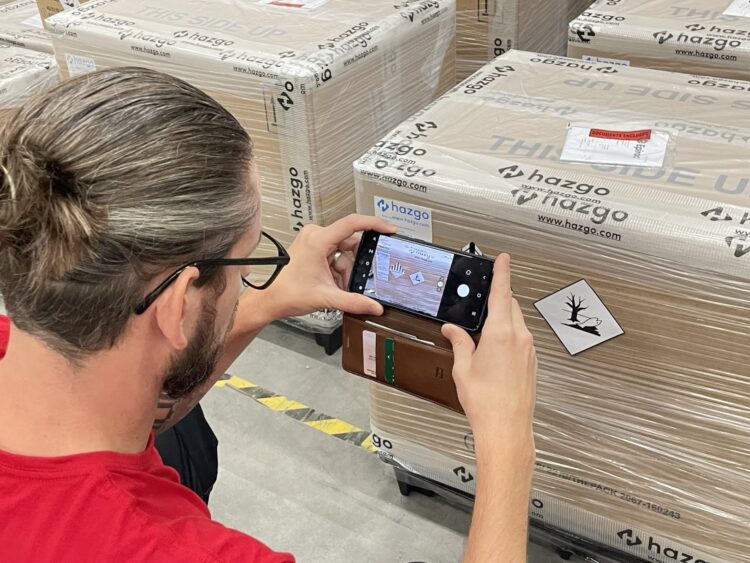 A man uses a cell phone to check labels on a cargo shipment