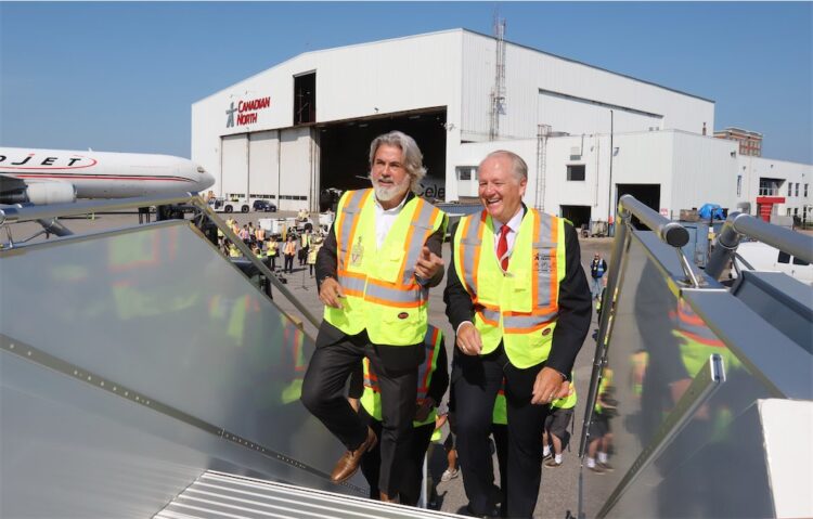 Two men in yellow vests walk up an outdoor staircase at YOW in front of a Canadian North warehouse