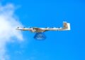 A Wing drone carries a Walmart package against a blue sky