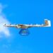 A Wing drone carries a Walmart package against a blue sky