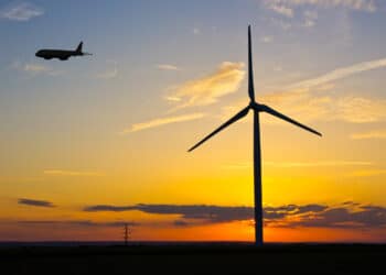 A plane flies past a windmill at dusk