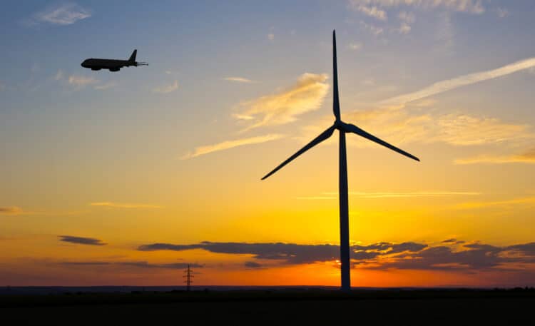 A plane flies past a windmill at dusk