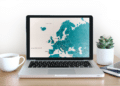 A map of Europe displayed on a laptop atop a desk with coffee cup and plant
