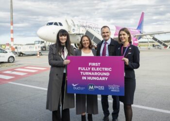 Four people hold a sign reading "first fully electric turnaround in Hungary" in front of a Wizz Air plane on the tarmac