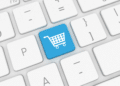 A white computer keyboard with one blue key showing a shopping cart