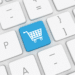 A white computer keyboard with one blue key showing a shopping cart