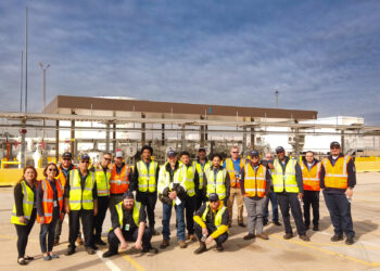 A group of people in orange and yellow vests pose in front of a fuel facility