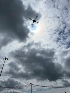 A drone flies above power lines in a cloudy sky