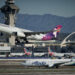 Hawaiian Airlines plane takes off while Alaska Airlines plane sits on tarmac