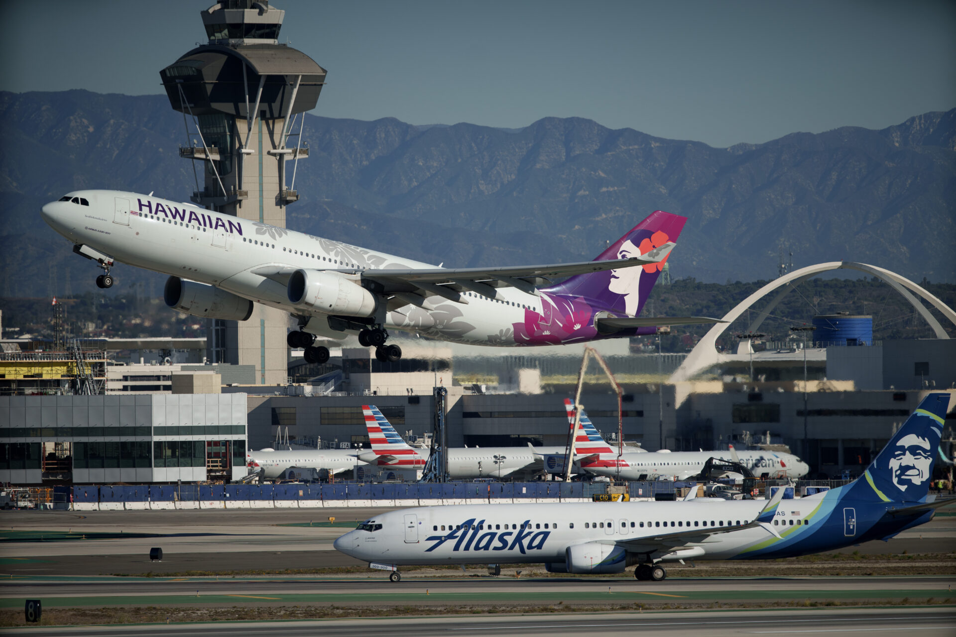 Hawaiian Airlines plane takes off while Alaska Airlines plane sits on tarmac