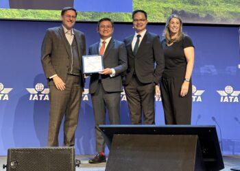 Four people stand in front of an IATA screen, with the person second from left holding a certificate of recognition