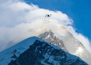 A drone flies above a mountain, shrouded in mist, cloud and snow