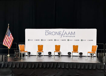 Empty chairs on a stage in front of a sign reading "FAA Drone / AAM Symposium"