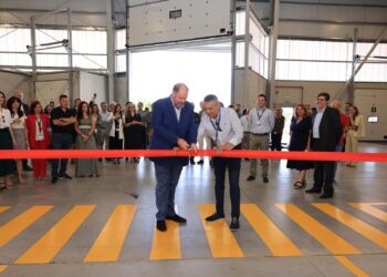 Two men cut a red ribbon in a warehouse filled with people