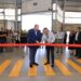 Two men cut a red ribbon in a warehouse filled with people