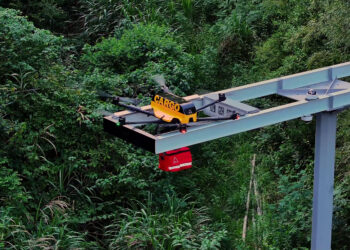 A drone carrying a package on a metal frame at tree level