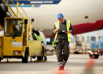 A man consults a tablet as he walks in front of a plane and ground support equipment